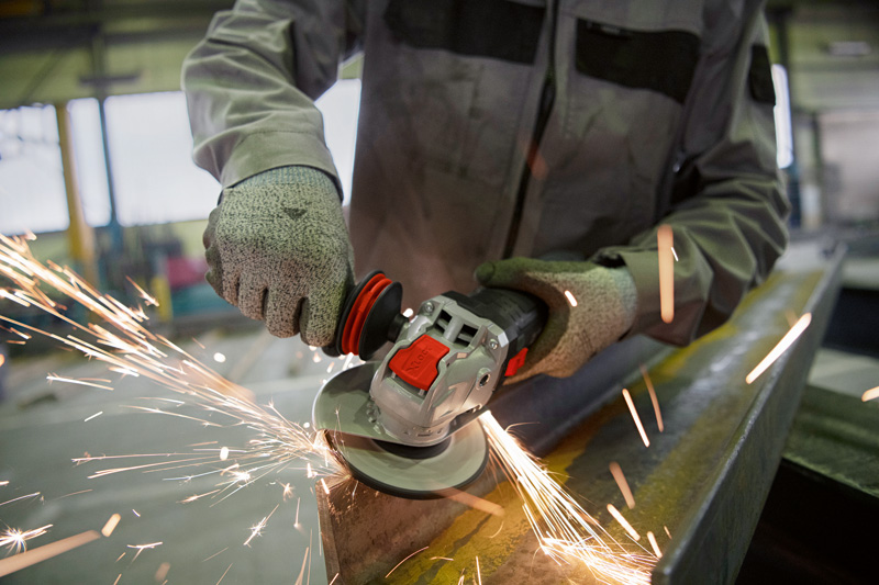 Eine Person mit Schutzausrüstung schleift Metall mit einem Winkelschleifer, wobei Funken entstehen. Anwendungsbild