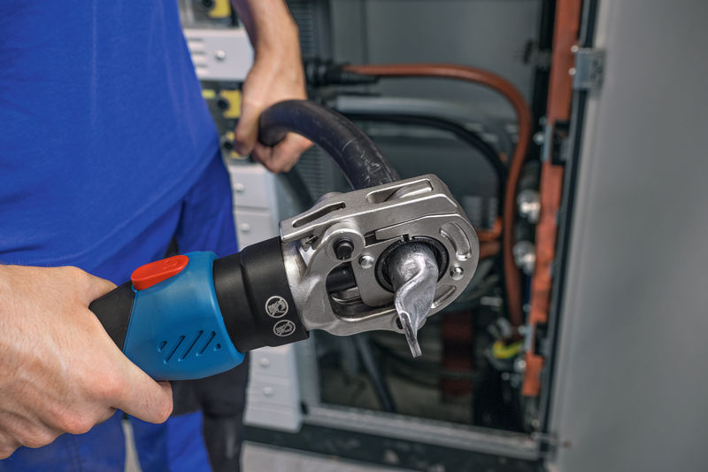 Eine Person verwendet ein kabelloses hydraulisches Crimpwerkzeug an einem dicken Kabel in der Nähe von Schalttafeln. Anwendungsbild