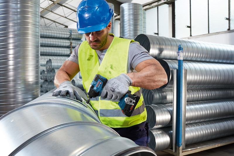 Eine Person mit Sicherheitsausrüstung befestigt Metallrohrleitungen mit einem Akku-Elektrowerkzeug. Anwendungsbild