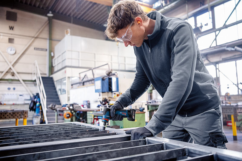 Eine Person mit Schutzausrüstung verwendet einen Rotationsschleifer an einem Metallrahmen. Anwendungsbild