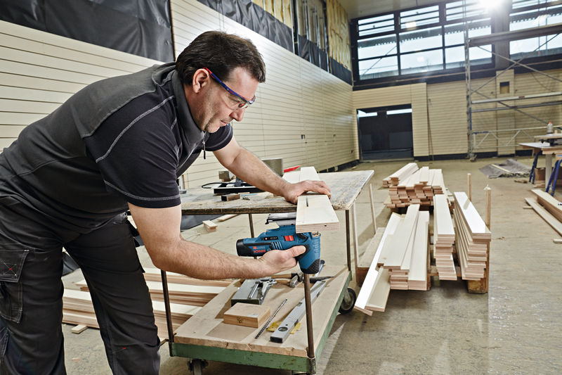 Eine Person mit Schutzausrüstung schneidet in einer Werkstatt mit einer Akku-Stichsäge Holz. Anwendungsbild