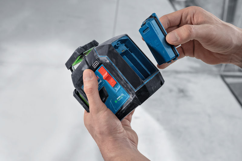 Person wechselt auf einer Baustelle die Batterie in einem Lasernivelliergerät. Anwendungsbild