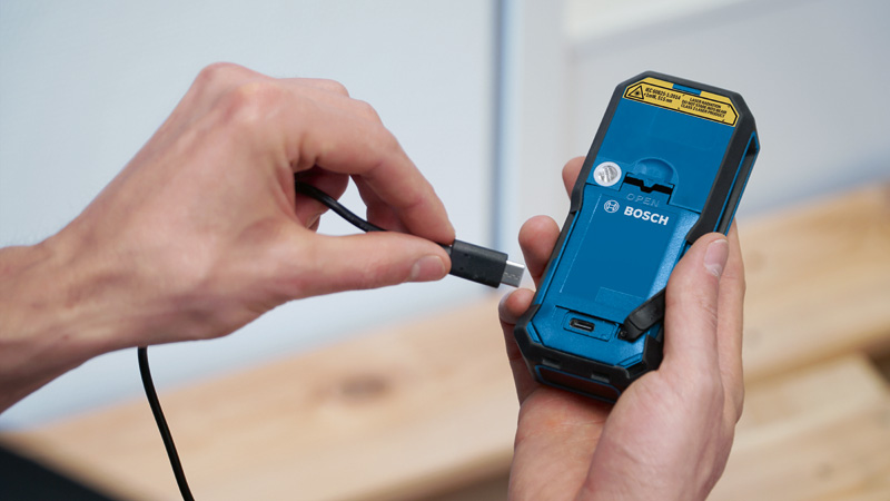 Eine Person schließt ein Ladekabel an der Rückseite eines handgeführten Elektrowerkzeugs an. Anwendungsbild
