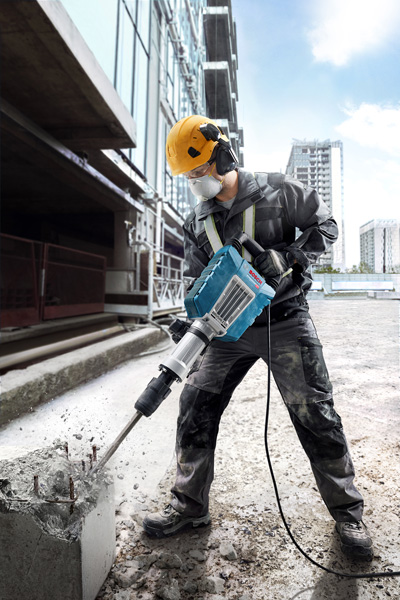 Eine Person mit Sicherheitsausrüstung bedient einen Brecher, um auf einer Baustelle Beton abzureißen. Anwendungsbild