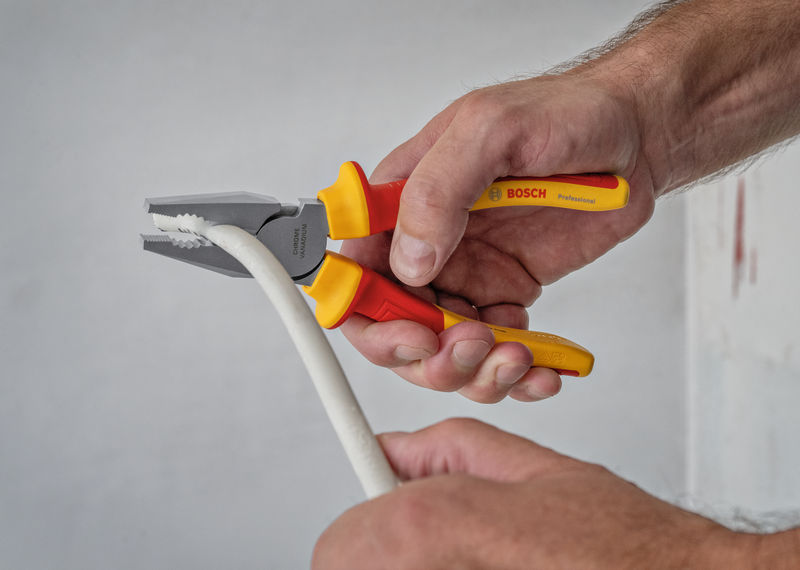 Eine Person greift und biegt mit einer isolierten Zange ein dickes weißes Kabel. Anwendungsbild