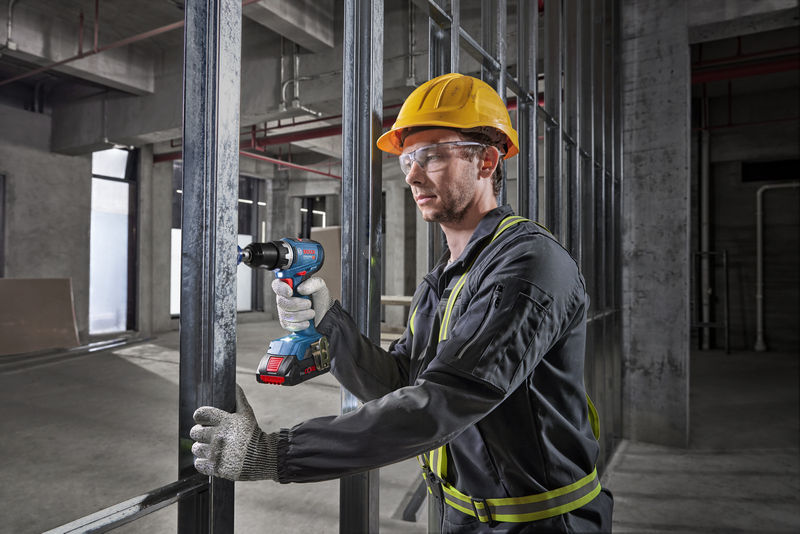Eine Person mit Schutzausrüstung bedient mit einer Akku-Bohrmaschine einen Metallrahmen. Anwendungsbild