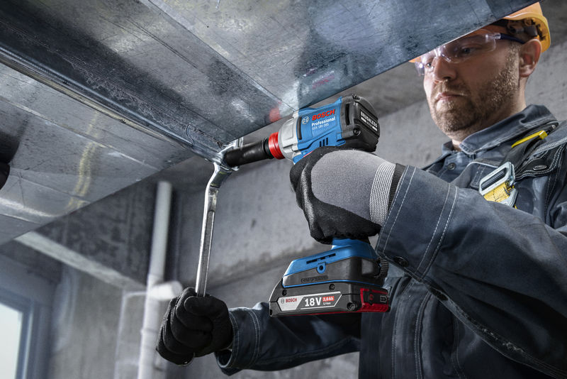 Eine Person mit Sicherheitsausrüstung befestigt mit einer Akku-Bohrmaschine einen Metallkanal. Anwendungsbild Nahaufnahme