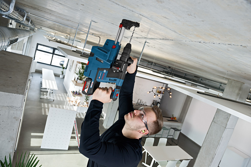Eine Person mit Sicherheitsausrüstung bohrt in einer modernen Arbeitsumgebung in eine Betondecke. Anwendungsbild