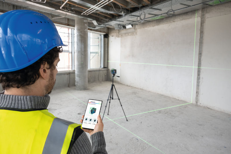 Eine Person mit Sicherheitsausrüstung bedient auf einer Baustelle ein Lasernivelliergerät aus der Ferne. Anwendungsbild