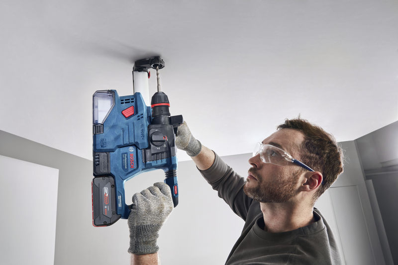 Eine Person mit Schutzausrüstung bohrt mit einem Bohrhammer in eine Decke. Anwendungsbild