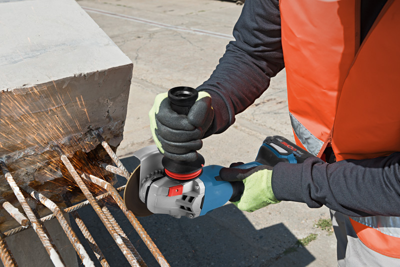 Eine Person mit Sicherheitsausrüstung schneidet mit einem Winkelschleifer Metallbewehrungsstäbe aus Beton. Anwendungsbild