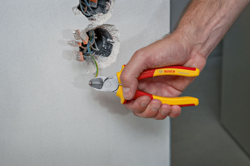 Eine Person verwendet eine isolierte Zange, um ein grünes Kabel aus einer elektrischen Wanddose zu schneiden. Anwendungsbild