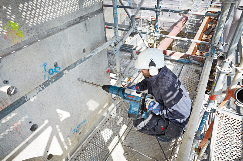 Eine Person mit Schutzausrüstung bohrt mit einem großen Bohrhammer in Beton. Anwendungsbild