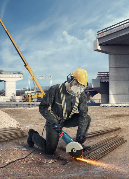 Eine Person mit Sicherheitsausrüstung verwendet auf einer Baustelle einen Winkelschleifer, um Metallstangen zu schneiden. Anwendungsbild