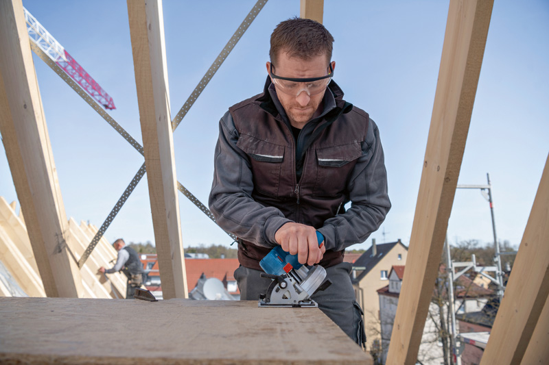 Eine Person mit Sicherheitsausrüstung verwendet eine Motorsäge, um auf einer Baustelle Holz zu schneiden. Anwendungsbild