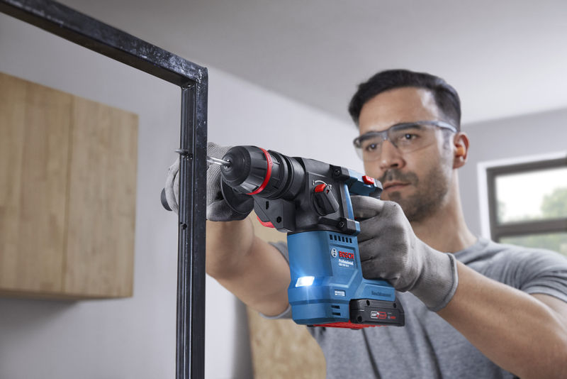 Eine Person mit Schutzausrüstung bohrt mit einem Akku-Bohrhammer in einen Metallrahmen. Anwendungsbild