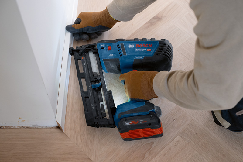 Eine Person mit Sicherheitsausrüstung befestigt mit einem Akku-Holznagler Zierleisten am Boden. Anwendungsbild