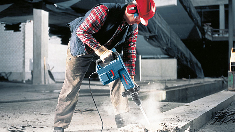 Eine Person mit Sicherheitsausrüstung bedient einen Abbruchhammer, um Beton aufzubrechen. Anwendungsbild