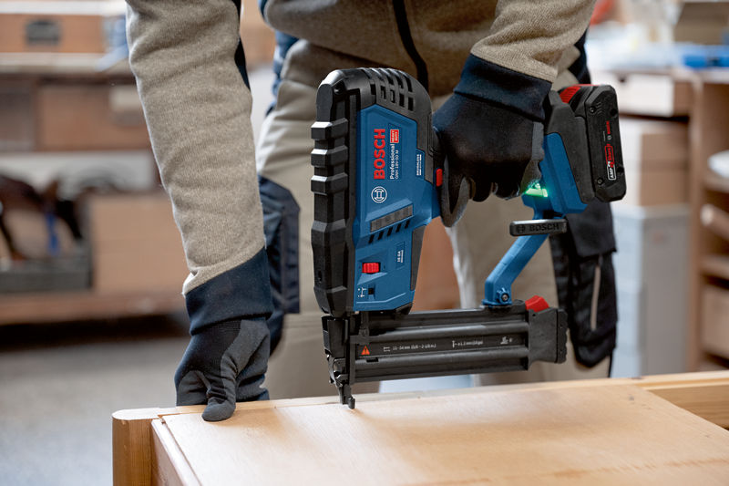 Eine Person mit Sicherheitsausrüstung verwendet einen kabellosen Holznagler auf einer Holzoberfläche. Anwendungsbild