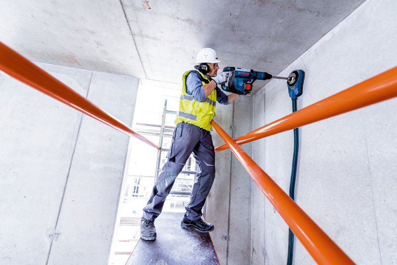 Eine Person mit Schutzausrüstung bohrt mit einem Bohrhammer in eine Betondecke. Anwendungsbild