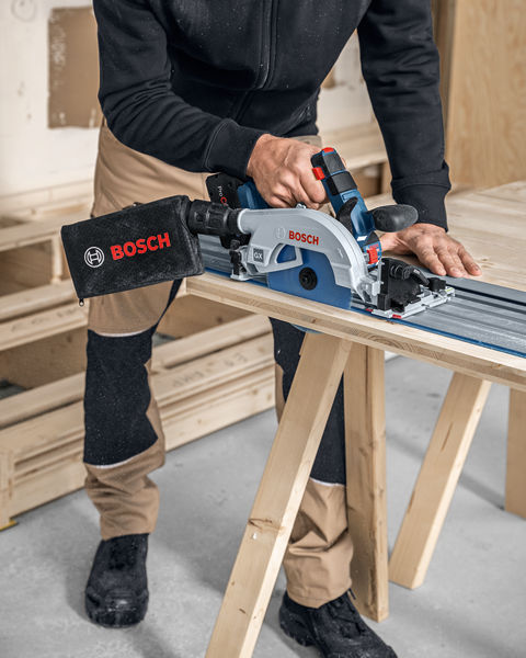 Eine Person mit Schutzausrüstung schneidet Holz mit einer Akku-Kreissäge auf einer Führungsschiene. Anwendungsbild