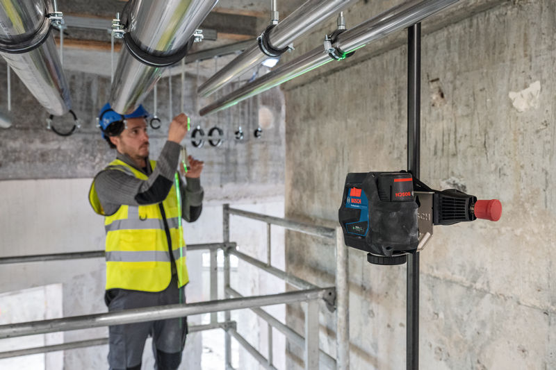 Eine Person mit Sicherheitsausrüstung richtet Rohre auf einer Baustelle mithilfe eines Lasernivelliergeräts aus. Anwendungsbild