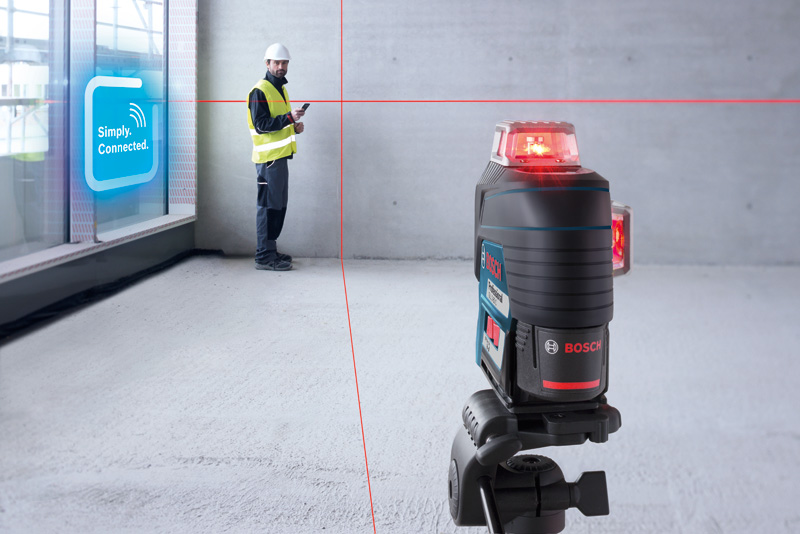 Eine Person mit Sicherheitsausrüstung verwendet ein Lasernivelliergerät, das rote Linien in einen modernen Raum projiziert. Anwendungsbild