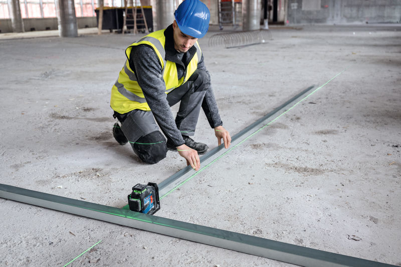 Eine Person mit Sicherheitsausrüstung richtet Metallträger mit einem Lasernivelliergerät aus. Anwendungsbild