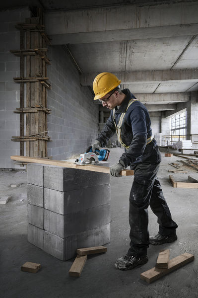 Eine Person mit Sicherheitsausrüstung schneidet auf einer Baustelle mit einer Kreissäge Holz. Anwendungsbild
