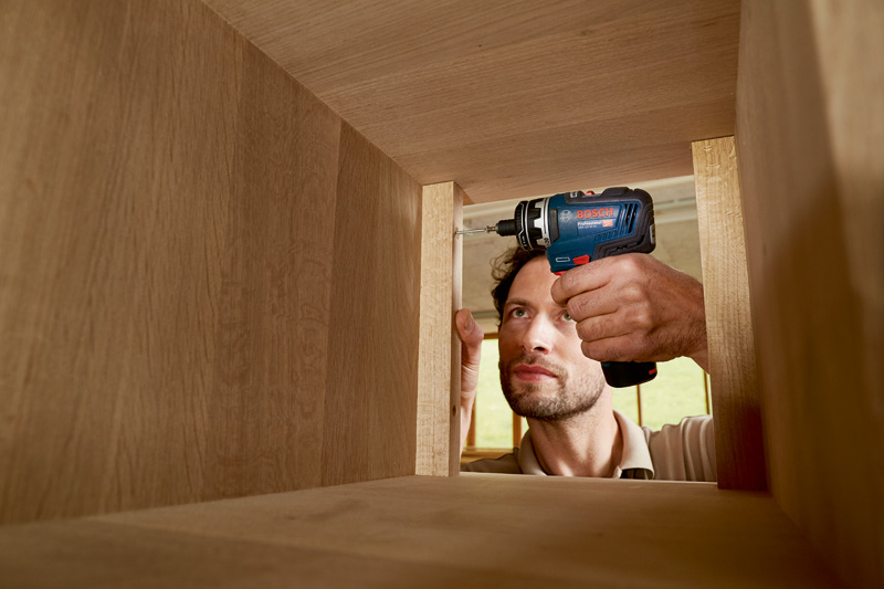 Eine Person verwendet eine Akkubohrmaschine, um einen Holzschrank zusammenzubauen. Anwendungsbild