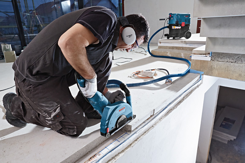 Eine Person mit Sicherheitsausrüstung verwendet eine Mauernutfräse auf Beton in der Nähe eines Vakuumsystems. Anwendungsbild