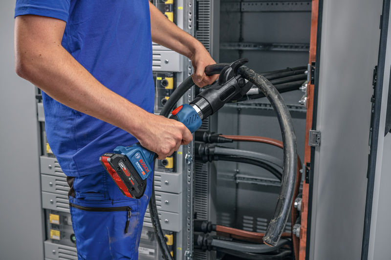 Eine Person mit Sicherheitsausrüstung verwendet ein kabelloses hydraulisches Schneidwerkzeug an dicken Kabeln. Anwendungsbild