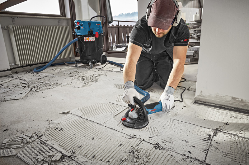 Eine Person mit Sicherheitsausrüstung schleift Betonböden mit einem Betonschleifer. Anwendungsbild