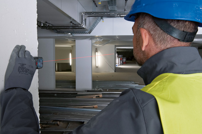 Eine Person mit Sicherheitsausrüstung misst die Entfernung auf einer Baustelle mit einem Lasermessgerät. Anwendungsbild
