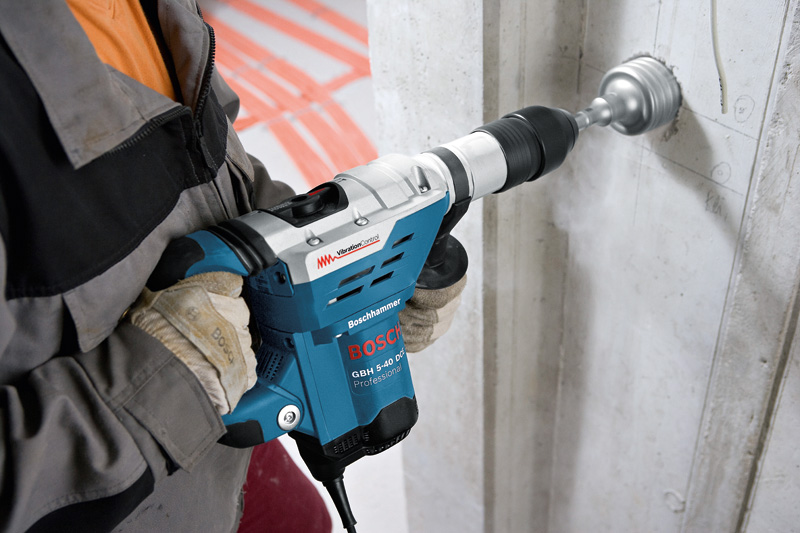 Eine Person mit Schutzausrüstung bohrt mit einem Bohrhammer in eine Betonwand. Anwendungsbild
