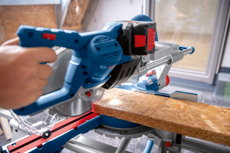 Person schneidet ein Holzbrett mit einer Akku-Gehrungssäge auf einer Werkbank. Anwendungsbild