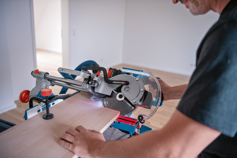 Eine Person verwendet eine kabellose Gehrungssäge mit einem Lasernivellierungswerkzeug, um Holz zu schneiden. Anwendungsbild