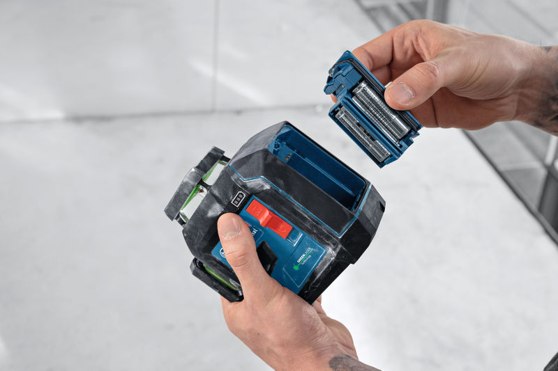 Eine Person tauscht die Batterien in einem Lasernivelliergerät im Innenbereich aus. Anwendungsbild