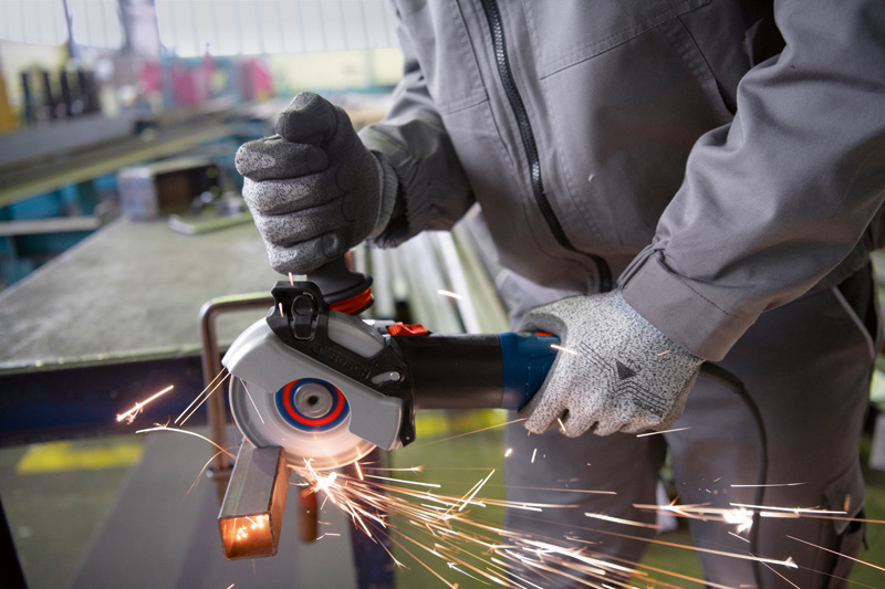 Eine Person mit Schutzausrüstung schleift eine Metallstange mit einem handgeführten Winkelschleifer. Anwendungsbild