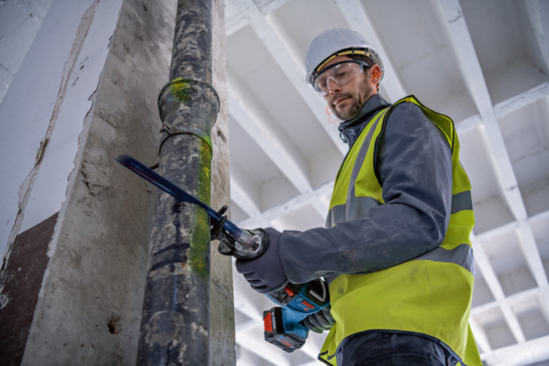 Eine Person mit Sicherheitsausrüstung schneidet mit einer Säbelsäge ein Metallrohr. Anwendungsbild