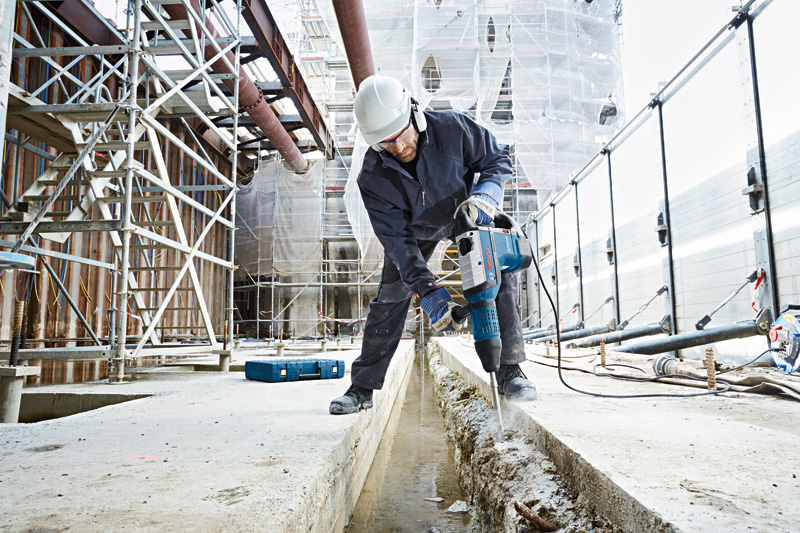 Eine Person mit Sicherheitsausrüstung verwendet einen Bohrhammer, um auf einer Baustelle Beton aufzubrechen. Anwendungsbild
