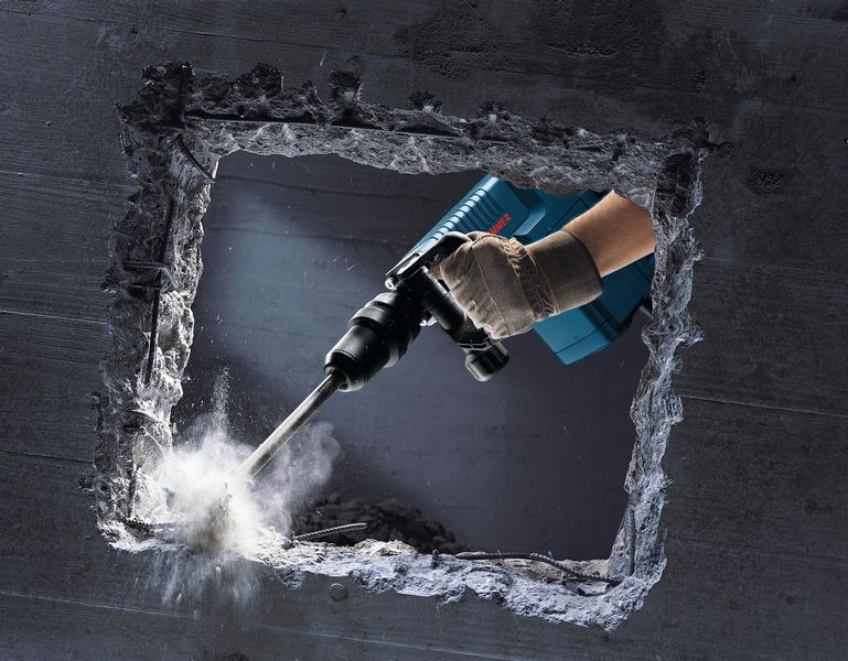 Eine Person mit Schutzausrüstung bohrt mit einem Bohrhammer durch eine Betonwand. Anwendungsbild