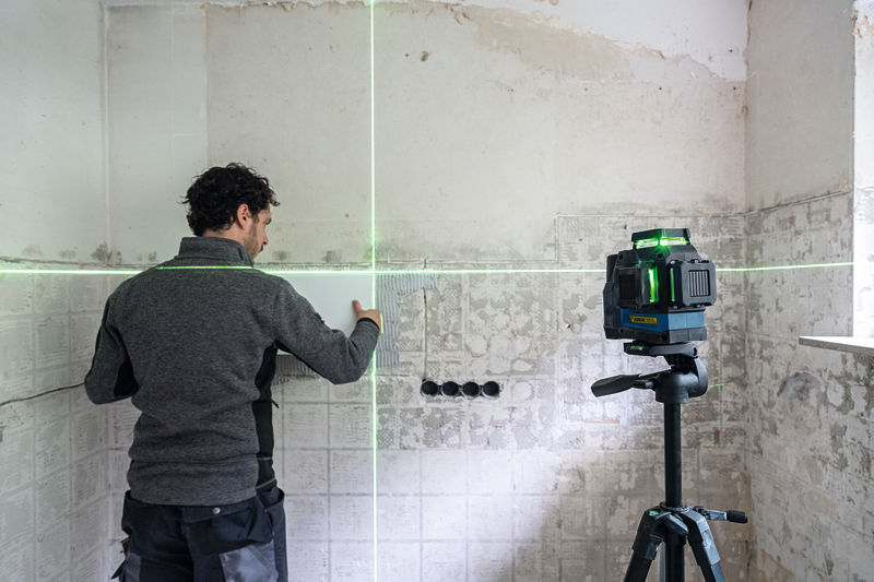 Person richtet Fliesen an einer Wand mit einem Lasernivelliergerät auf einem Stativ aus. Anwendungsbild