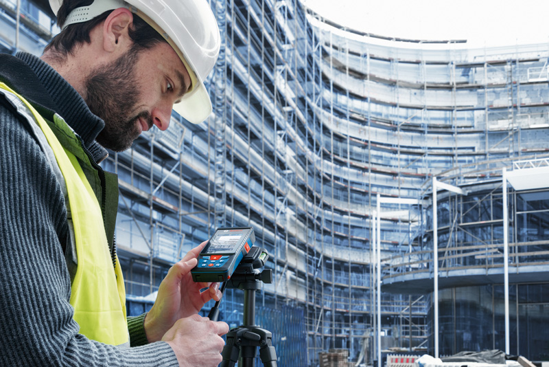 Eine Person mit Sicherheitsausrüstung verwendet auf einer Baustelle ein Lasermessgerät. Anwendungsbild