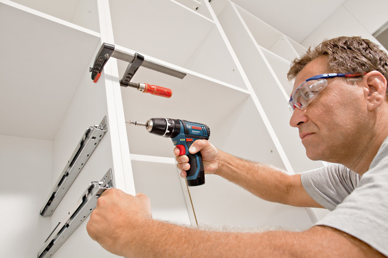 Eine Person mit Schutzausrüstung verwendet eine Akku-Bohrmaschine, um einen Schrank zusammenzubauen. Anwendungsbild
