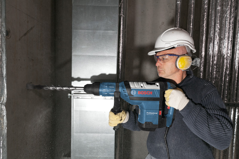 Eine Person mit Schutzausrüstung bohrt mit einem Bohrhammer in eine Betonwand. Anwendungsbild
