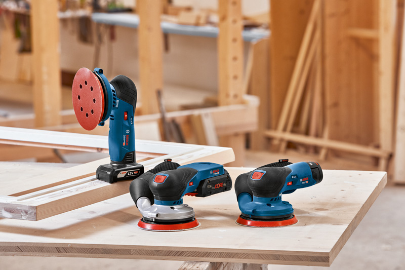 Drei elektrische Schleifmaschinen stehen auf einer Holzwerkbank in einer Tischlerei. Anwendungsbild