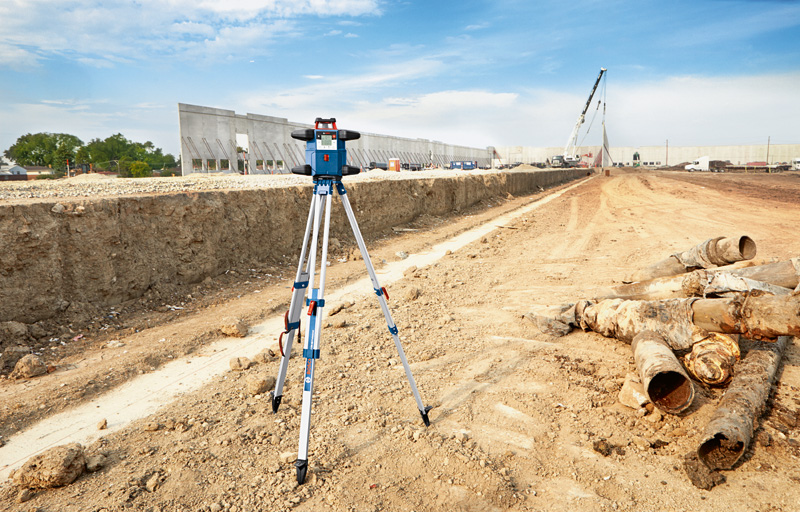 Auf einem Stativ aufgestelltes Lasernivelliergerät auf einer großen Baustelle. Anwendungsbild
