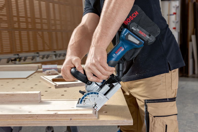 Eine Person mit Sicherheitsausrüstung verwendet eine Lamellofräse, um Holz auf einer Werkbank zu schneiden. Anwendungsbild