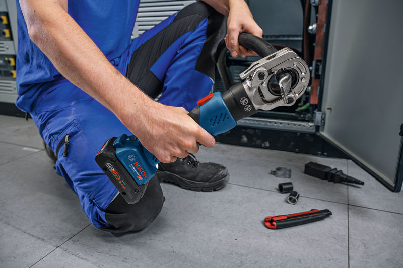 Eine Person mit Schutzausrüstung verwendet ein kabelloses hydraulisches Crimpwerkzeug in der Nähe von Schaltschränken. Anwendungsbild